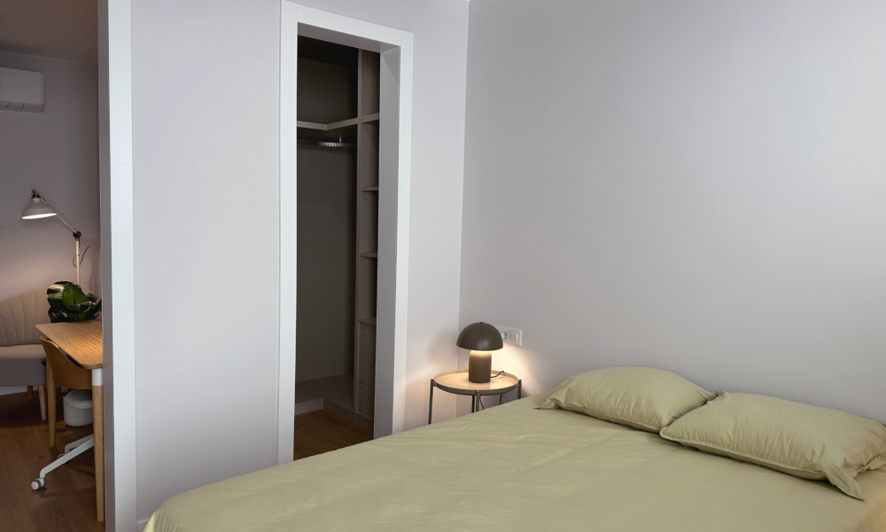 Cama de matrimonio con armario Cama de matrimonio con la puerta del armario abierta y parte del pasillo