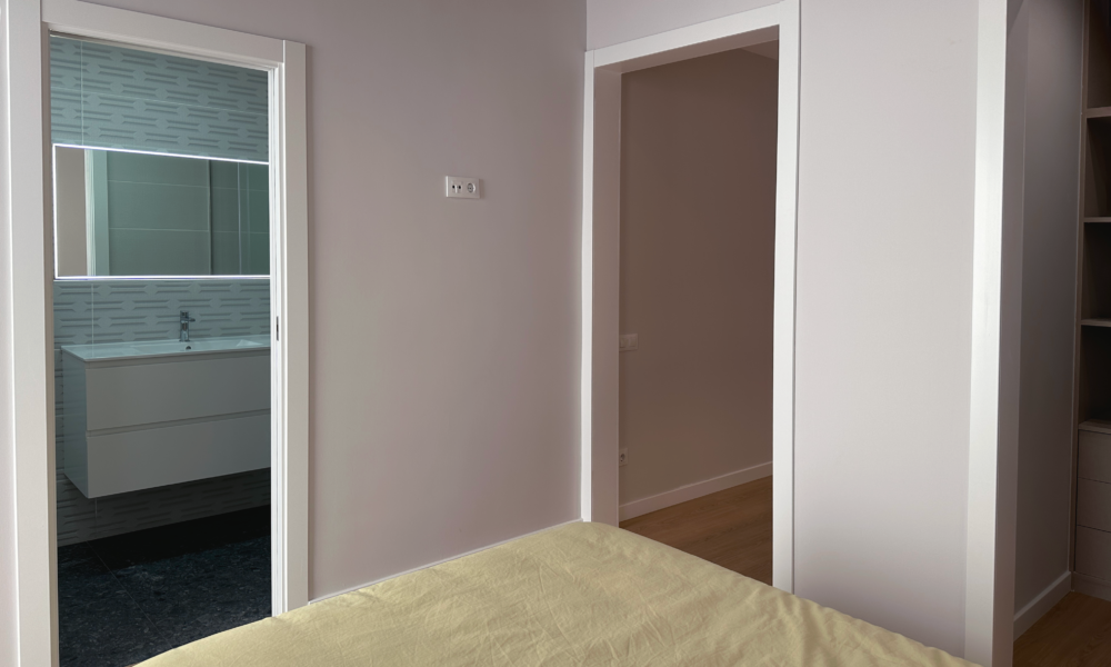 habitación pies de la cama con una vision parcial del baño y la puerta que va hacia el pasillo