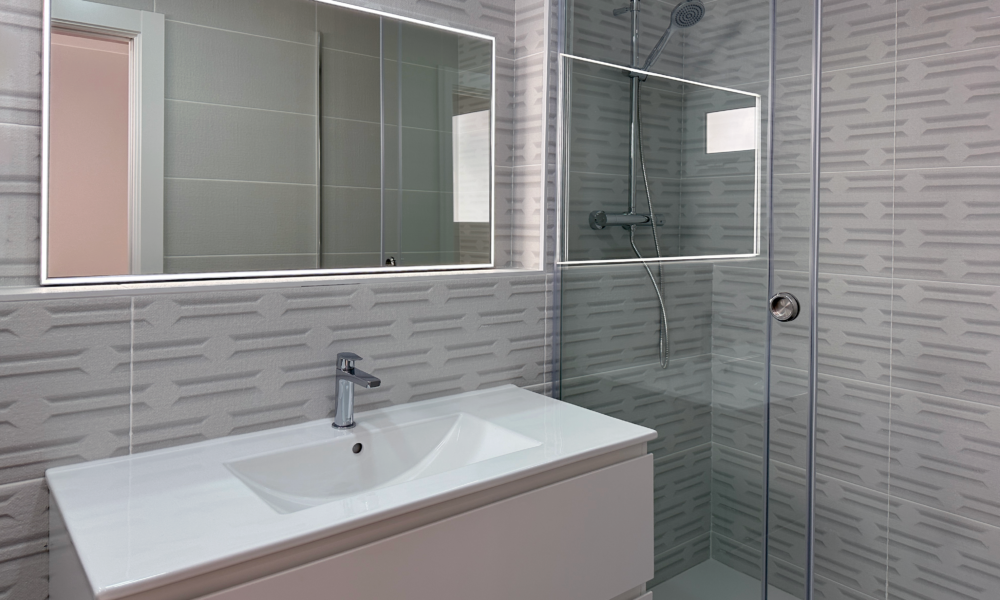 baño con plato de ducha Vision del segundo baño con un gran plato de ducha, espejo rectangular y grifería.